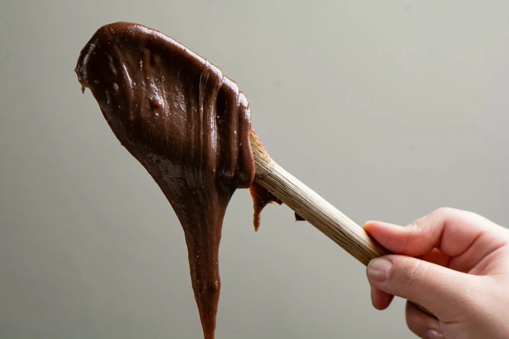 Espátula sustentando brigadeiro gourmet cremoso e brilhante caindo em bloco denso para demonstrar o ponto ideal de recheio para bolos.