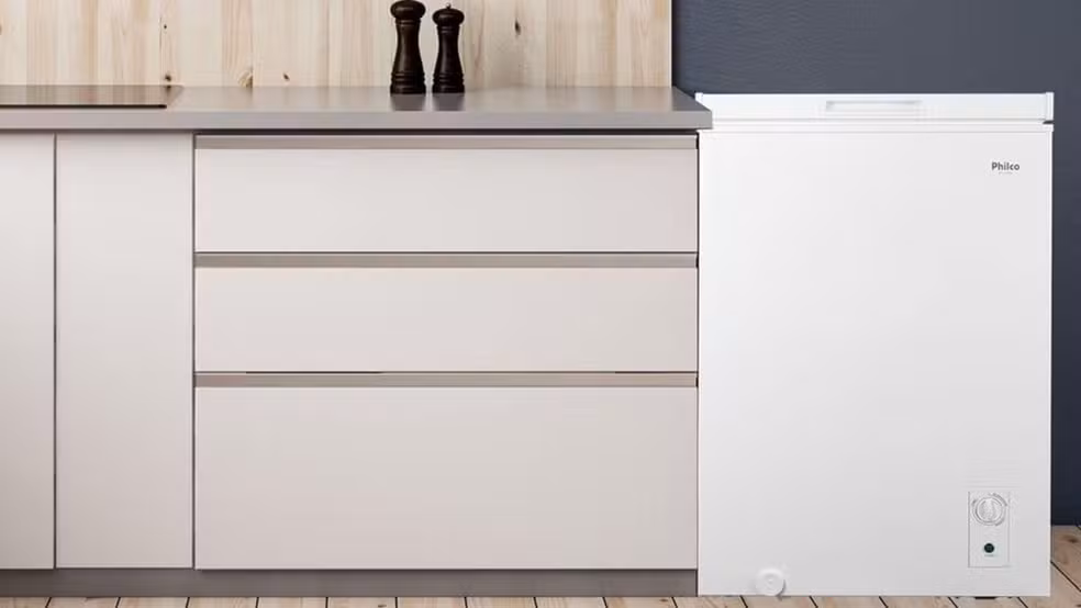 Freezer horizontal Philco branco posicionado ao lado de um balcão de cozinha planejado, destacando o painel de controle frontal para ajuste de temperatura.