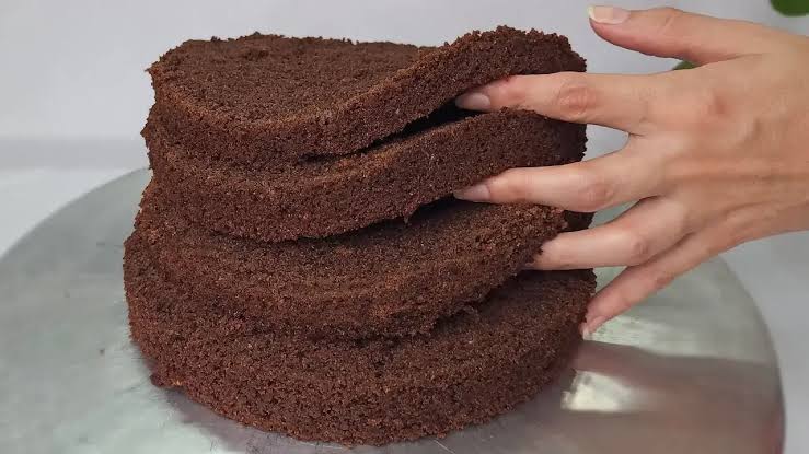 Mão pressionando suavemente discos de bolo de chocolate assado para demonstrar a maciez e a elasticidade da massa.