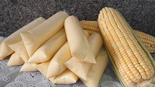 Geladinhos gourmet de milho verde cremosos com coloração amarelada natural, dispostos ao lado de espigas de milho fresco sobre uma mesa.