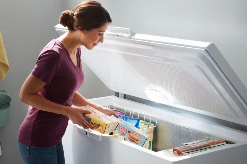 Mulher organizando embalagens de alimentos congelados dentro de um freezer horizontal branco aberto, ilustrando o espaço interno e a ausência de excesso de gelo.