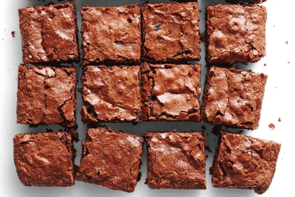 Doze brownies de chocolate cortados em quadrados, dispostos em um fundo branco, prontos para serem embalados para venda na rua.
