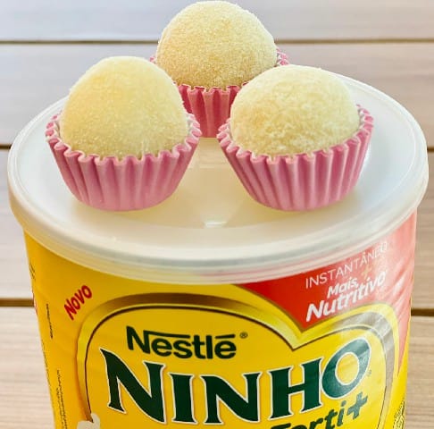 Três brigadeiros de leite Ninho em forminhas rosa, dispostos sobre a tampa de uma lata amarela de leite em pó.