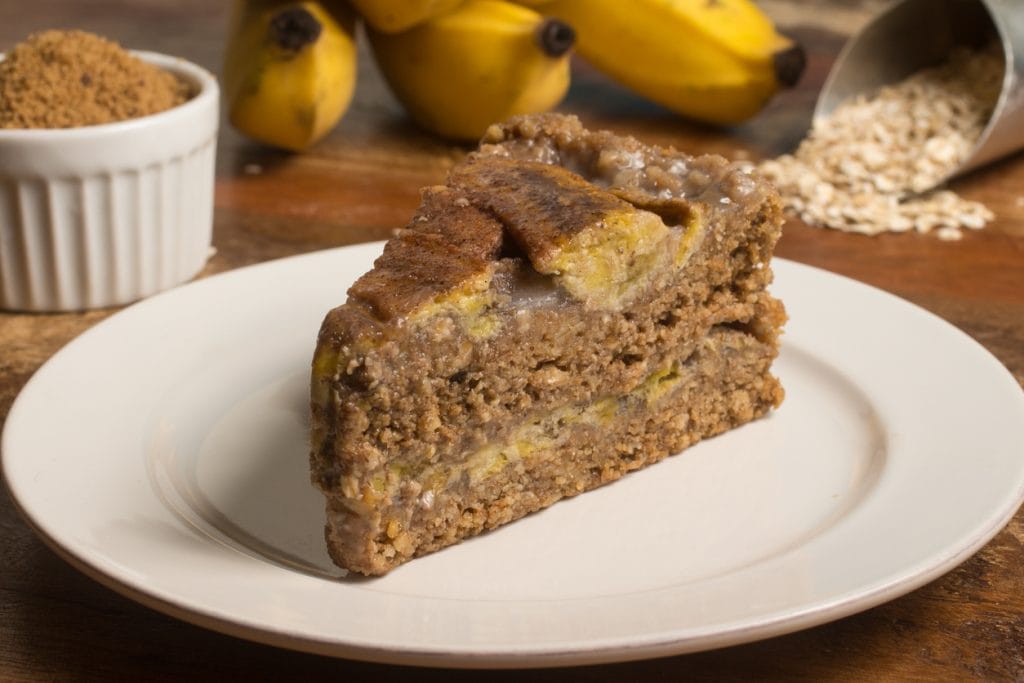 Uma fatia de bolo de banana com aveia em um prato branco, com textura densa e pedaços de banana visíveis na massa.