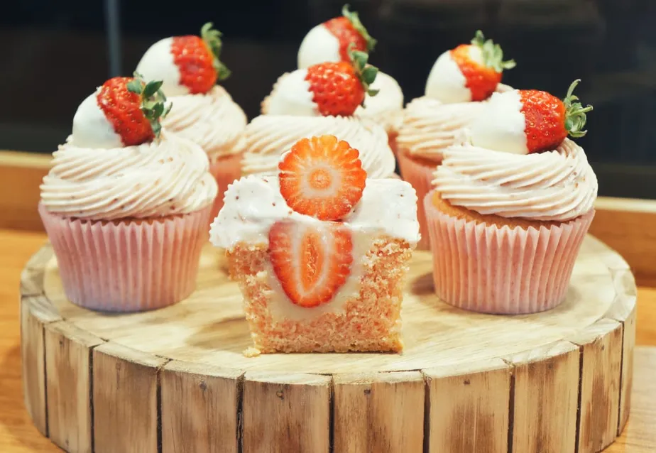 Vários cupcakes de morango com massa branca, cobertura de chantilly e morango fresco no topo.