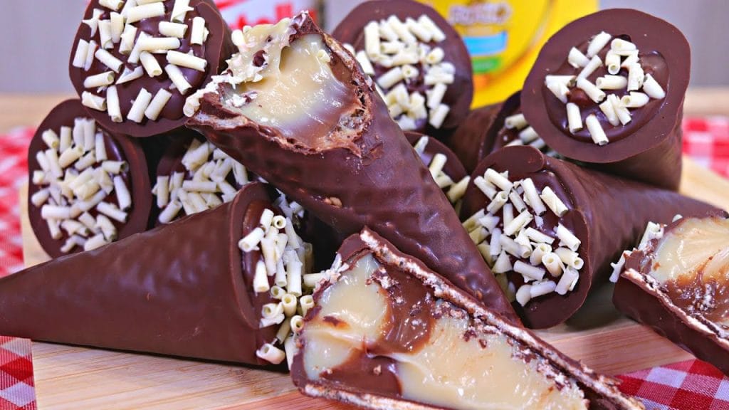 Uma pilha de mini cones de chocolate recheados com um creme branco, decorados com granulado de chocolate branco.