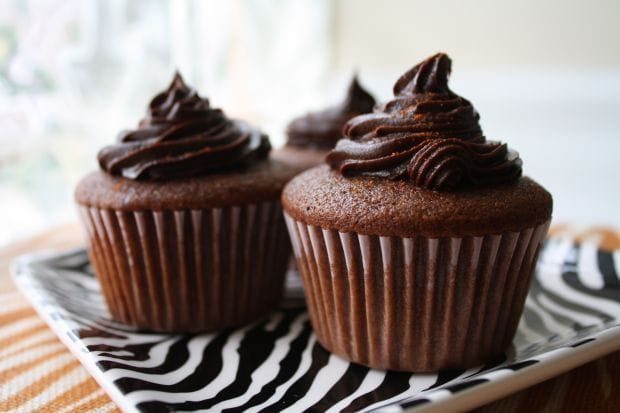 Três cupcakes de chocolate com cobertura cremosa, decorados com raspas de chocolate.