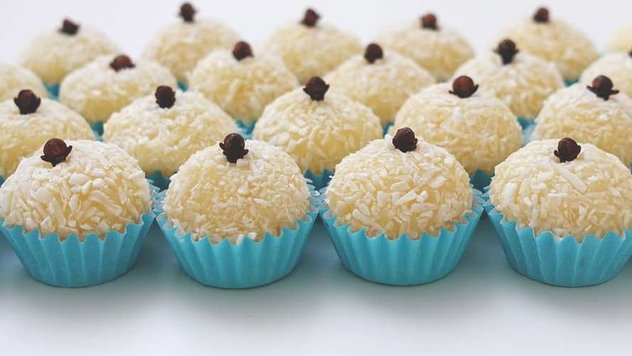 Uma coleção de beijinhos de coco, enrolados em coco ralado e decorados com um cravo-da-índia no topo de cada um.