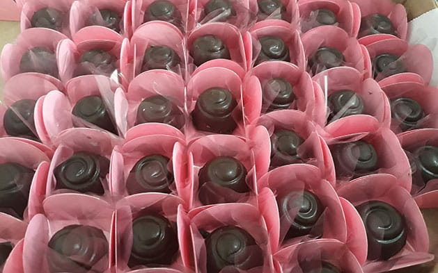 Várias mini trufas de chocolate com formato arredondado, embaladas em forminhas de papel cor de rosa.