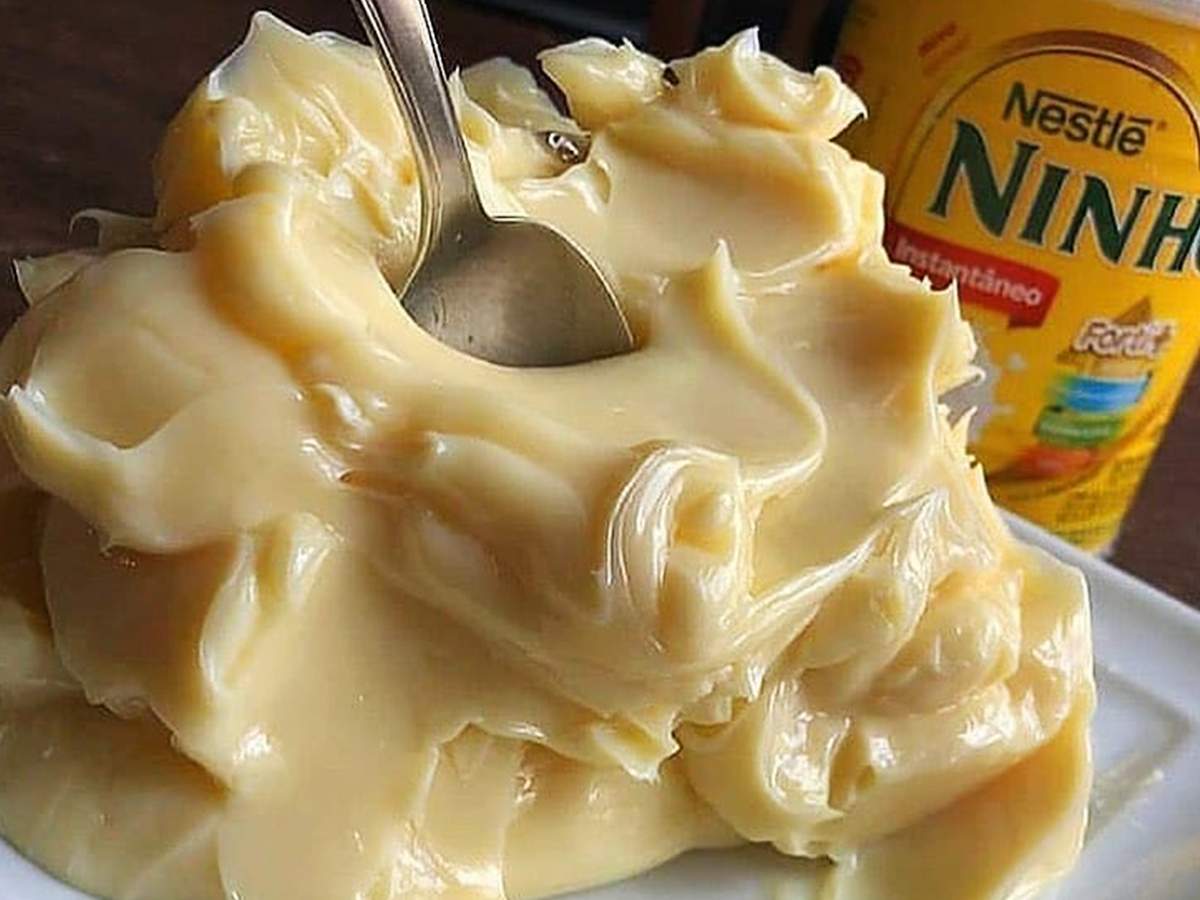 Uma tigela cheia de recheio cremoso e amarelo-claro de Leite Ninho, com uma colher inserida no creme, e uma embalagem de Leite Ninho ao fundo.