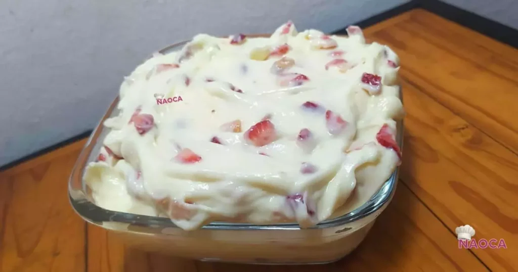 Uma tigela de vidro cheia de recheio cremoso de leite ninho, misturado com pedaços de morango vermelho picado e fresco.