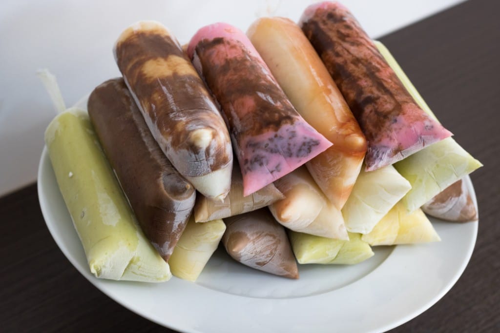 Pilha de dindins gourmet cremosos de diversos sabores (chocolate, morango, maracujá) dispostos em um prato branco, evidenciando a textura aveludada.