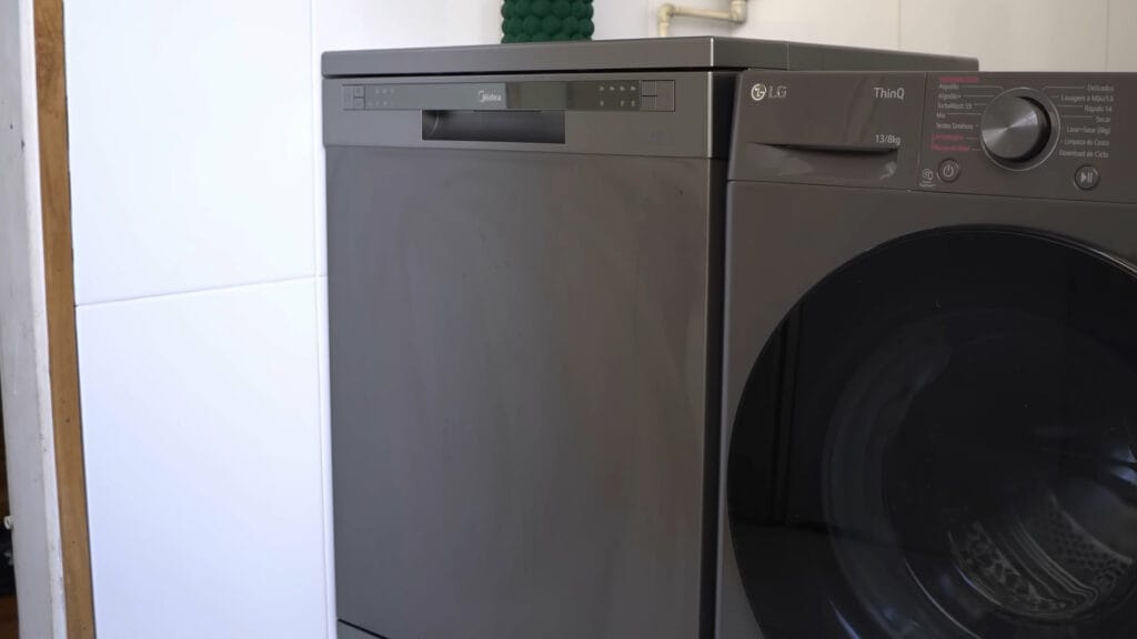 Vista lateral da lava-louças Midea 14 serviços preta instalada ao lado de uma lavadora de roupas, destacando o alinhamento e o acabamento superior do gabinete.