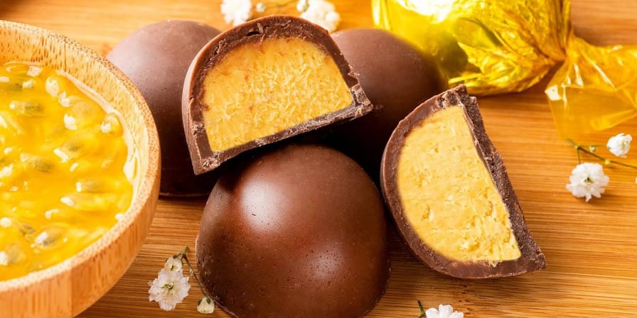 Trufas de chocolate de maracujá, uma delas cortada ao meio para mostrar o recheio amarelo e cremoso, ao lado de uma tigela com polpa da fruta.
