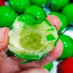 Foto de uma Uva do Amor (bombom recheado) cortada ao meio, mostrando o interior da uva verde e o recheio de brigadeiro branco cremoso.