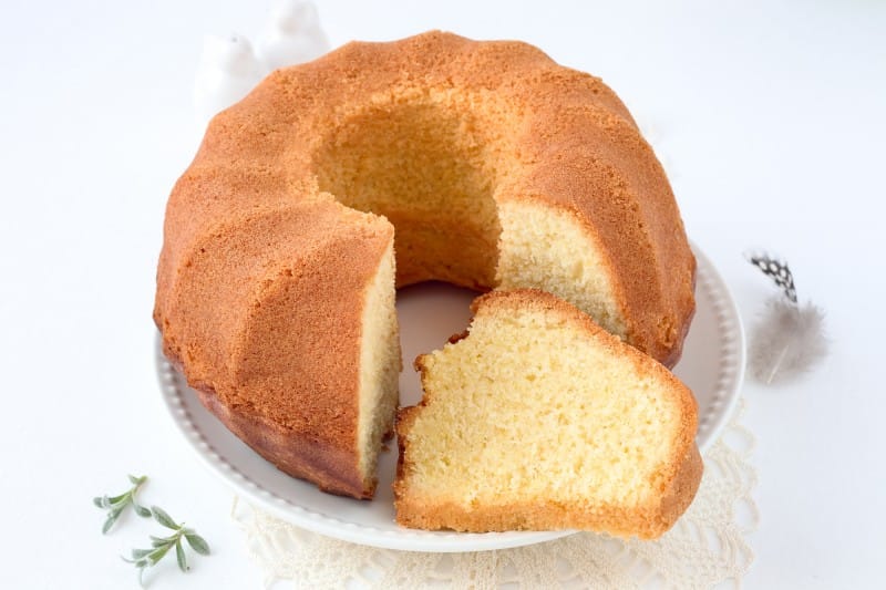 Um bolo de iogurte caseiro em um prato branco, com uma fatia cortada para mostrar a textura clara e macia da massa.