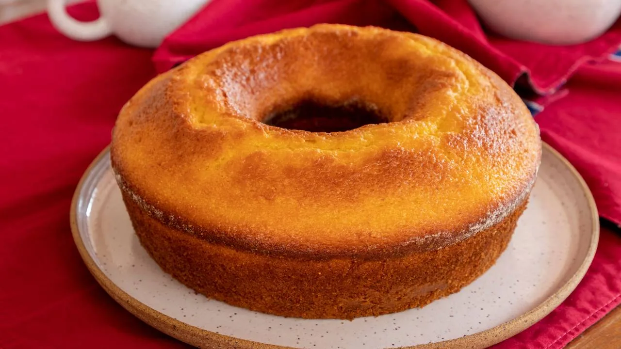 Bolo simples de liquidificador dourado e fofinho em um prato branco com borda rústica.