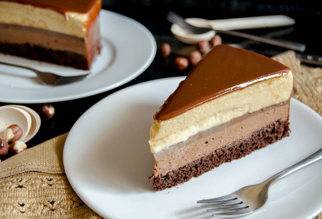 Uma fatia de entremet de chocolate e caramelo, mostrando as camadas de bolo, mousse de chocolate, mousse de caramelo e a cobertura de glacage espelhado.