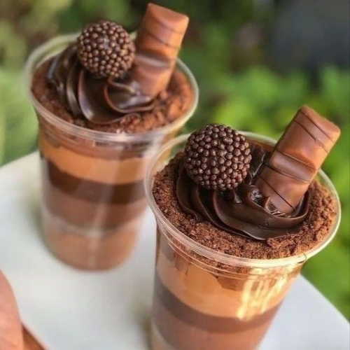 Dois Copos da Felicidade em camadas com diferentes texturas de brigadeiro de chocolate e farofa de chocolate, decorados com chantilly de chocolate, bolinha de chocolate e pedaço de Kinder Bueno. Ideal para confeitaria, doces para festas e venda.