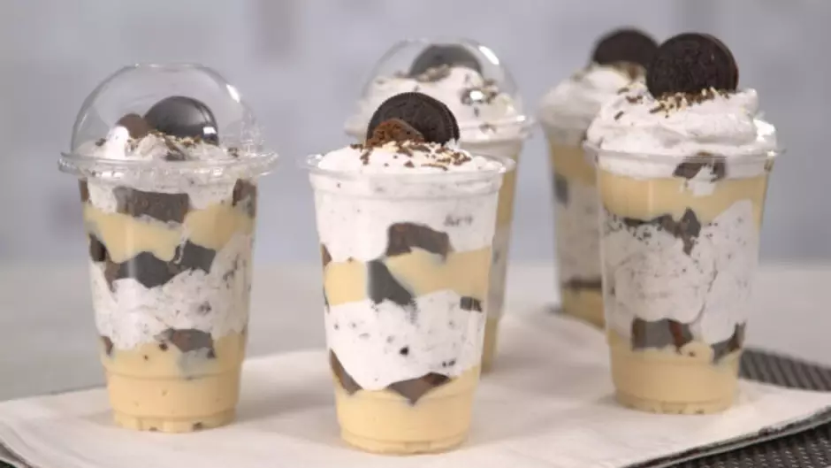 Vários Copos da Felicidade com camadas de creme branco e pedaços de biscoito Oreo, cobertos com chantilly e um biscoito Oreo inteiro. Ideal para receitas de Copo da Felicidade Oreo, sobremesas e venda.