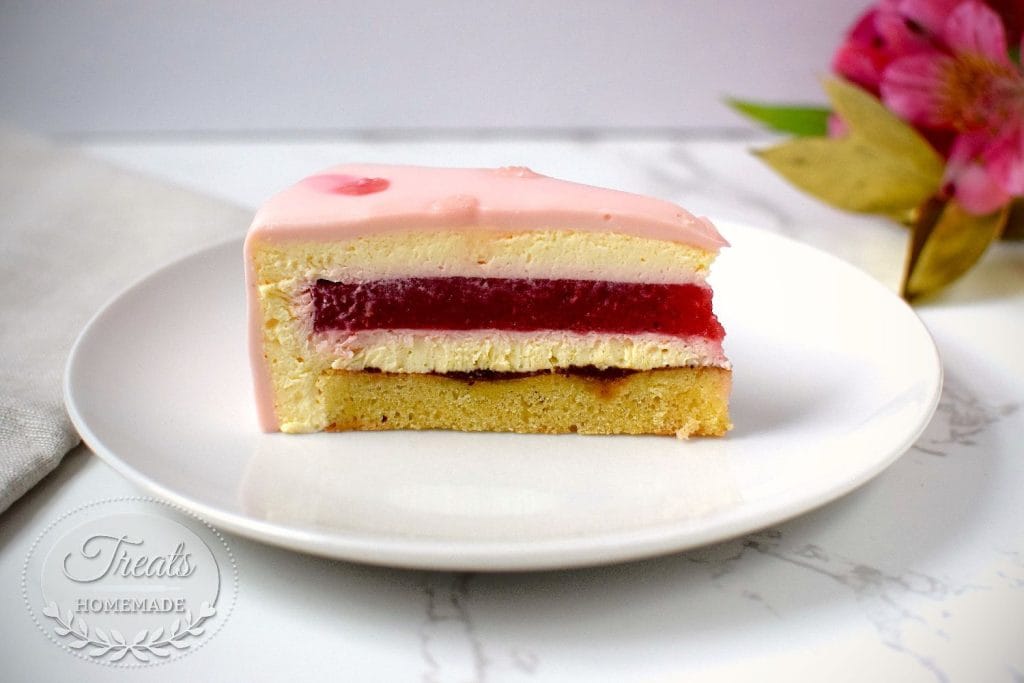Uma fatia de entremet de morango mostrando as camadas de bolo, creme, geleia vermelha e a mousse de morango, em um prato branco.