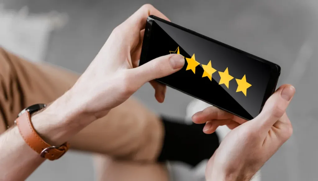 Mãos segurando um smartphone que exibe na tela uma avaliação de quatro estrelas, representando o feedback do consumidor em uma plataforma online.