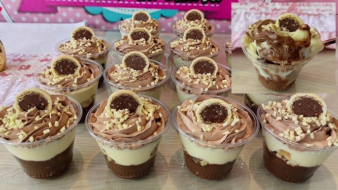 Muitos Copos da Felicidade em camadas com creme de chocolate, creme branco e pedaços de bombom Ouro Branco, decorados com chantilly de chocolate, raspas de chocolate branco e um bombom Ouro Branco em cima. Ideal para confeitaria, doces gourmet e eventos.