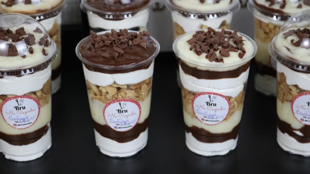 Vários Copos da Felicidade com camadas de brigadeiro de coco, pedaços de bolo de chocolate e creme branco, decorados com raspas de chocolate e coco queimado. Inclui rótulo personalizado. Ideal para confeitaria e venda.