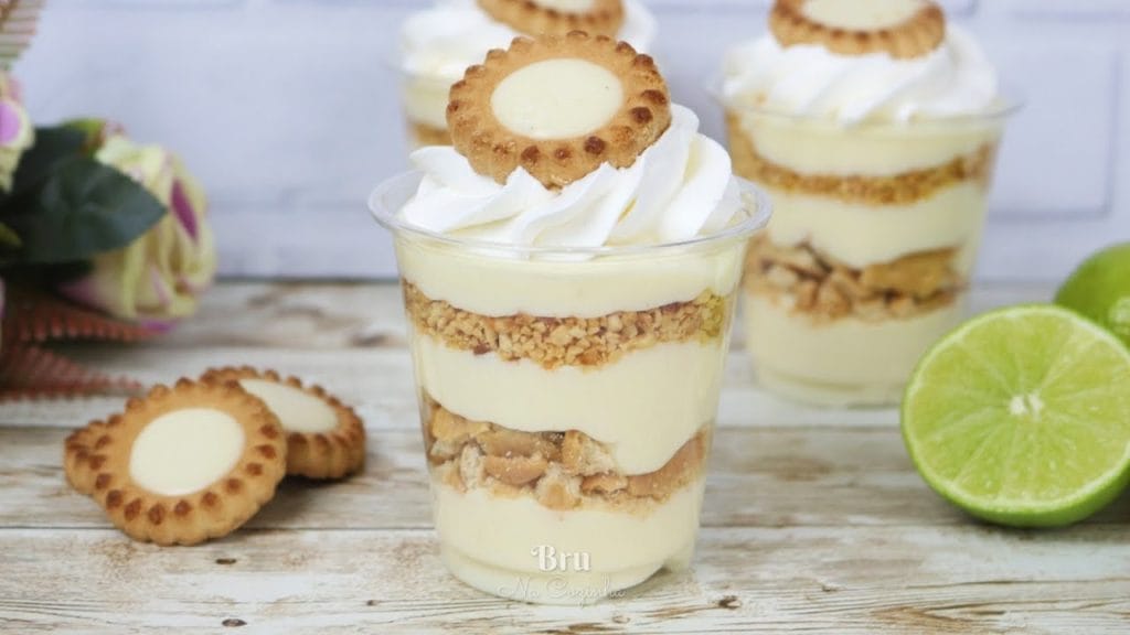 Vários Copos da Felicidade em camadas com creme de limão, pedaços de biscoito e merengue tostado, decorados com biscoitos redondos e raspas de limão. Ideal para confeitaria, sobremesas refrescantes e venda.