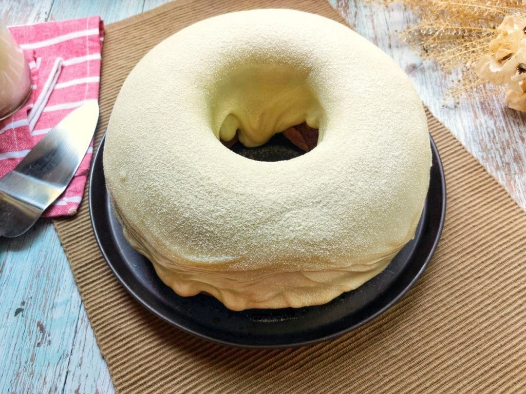 Um bolo de leite ninho com uma cobertura de glacê branco e espesso escorrendo pelo centro, sobre um prato preto. O bolo é polvilhado com leite ninho.