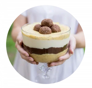 Taça da Felicidade em vidro, com camadas de creme de ninho e chocolate branco, decorada com chantilly e raspas de chocolate. Representa as opções delicadas e saborosas ensinadas.