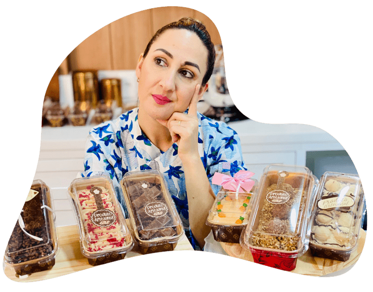 Confeiteira contemplando seis mini bolos caseirinhos embalados em caixas transparentes com rótulos de "Produto Artesanal", demonstrando profissionalismo