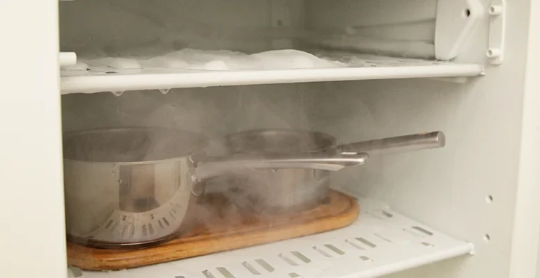 Demonstração segura de como descongelar freezer utilizando bacias com água quente para gerar vapor e soltar as placas de gelo sem danificar o aparelho.