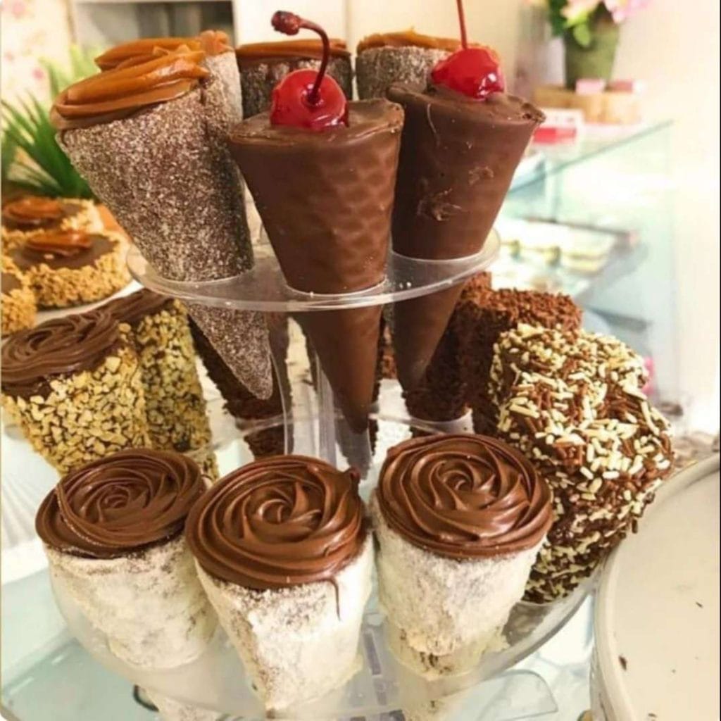 Expositor de cones trufados de chocolate com cereja e doce de leite, e bolinhos banhados em chocolate, usando técnicas de recheios e trufas