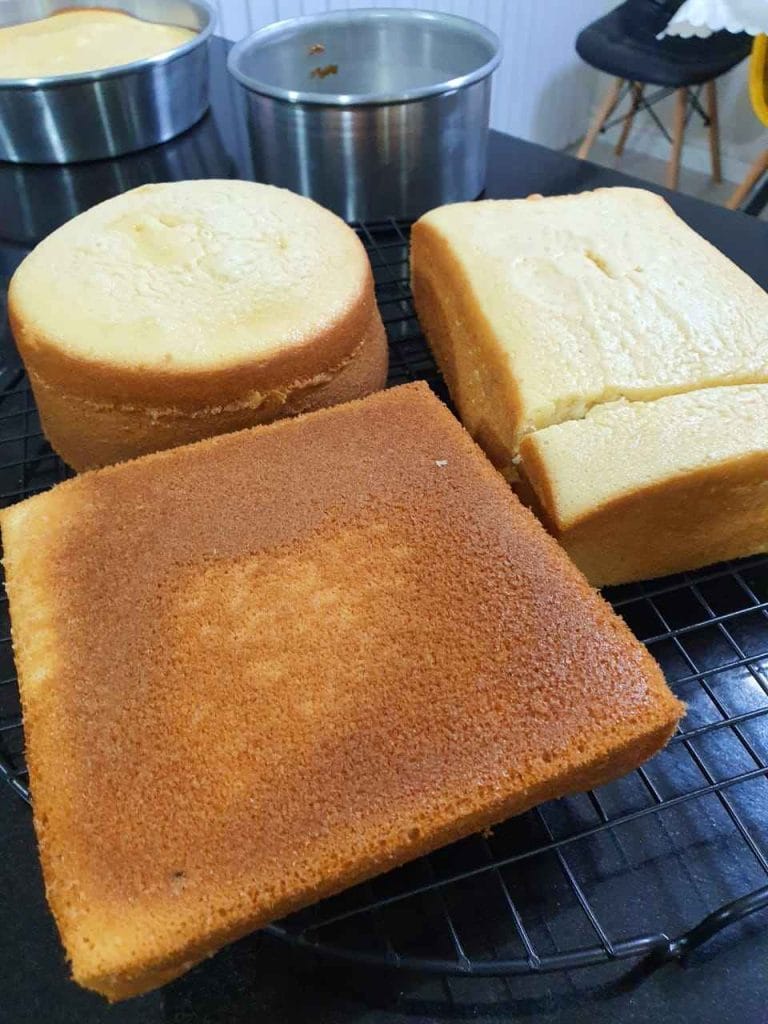 Três massas de bolo prontas (redonda e quadrada), mostrando a textura macia e a estrutura firme, conforme técnicas da apostila de massas perfeitas