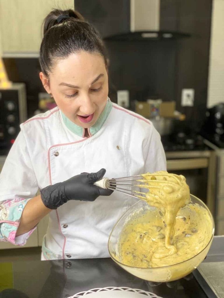 Chef confeiteira de uniforme e luvas misturando a massa de brownie com um fouet, mostrando a textura ideal para a casquinha crocante e miolo úmido