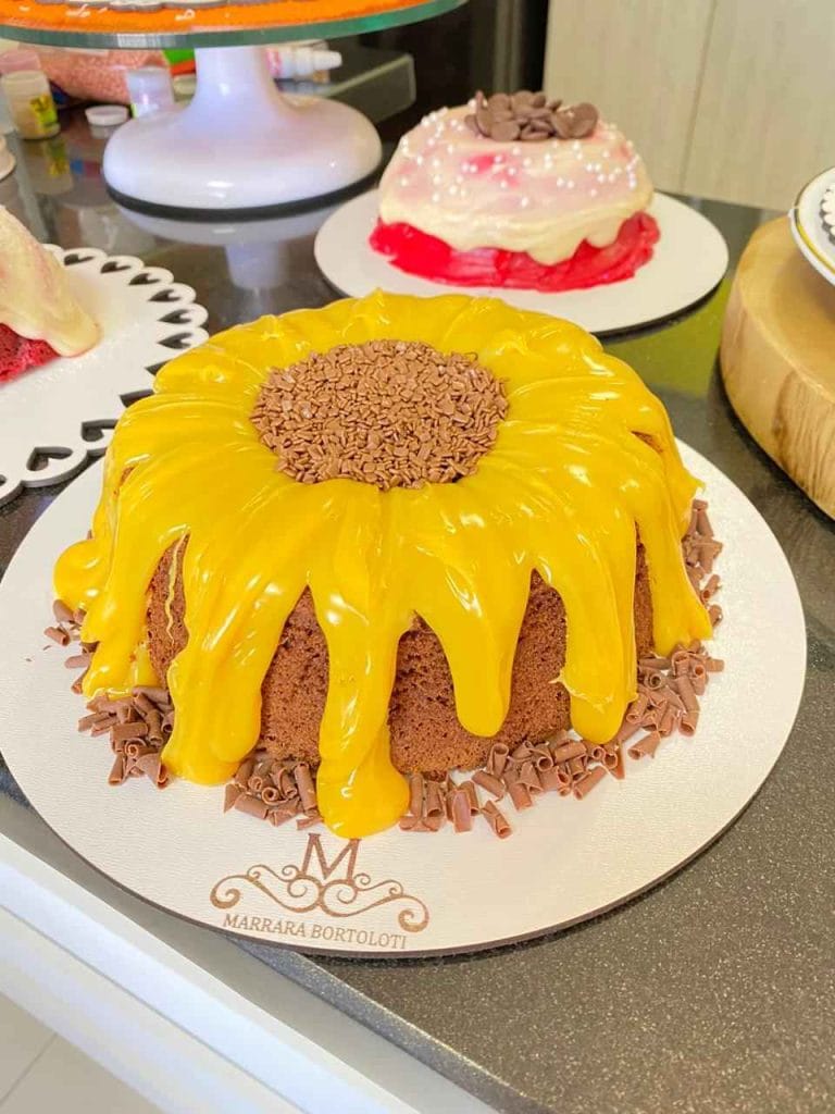 Bolo Vulcão de chocolate com cobertura de maracujá ou limão escorrendo (efeito piscina), raspas de chocolate e base decorada, conforme a apostila de bolos vulcão