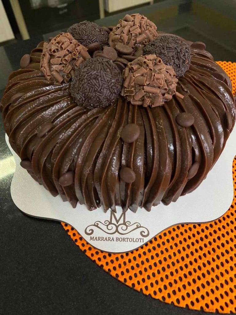 Bolo Vulcão totalmente coberto com chocolate cremoso (efeito vulcanizado) e decorado com brigadeiros gourmet e raspas de chocolate, ideal para apostila de bolos vulcão