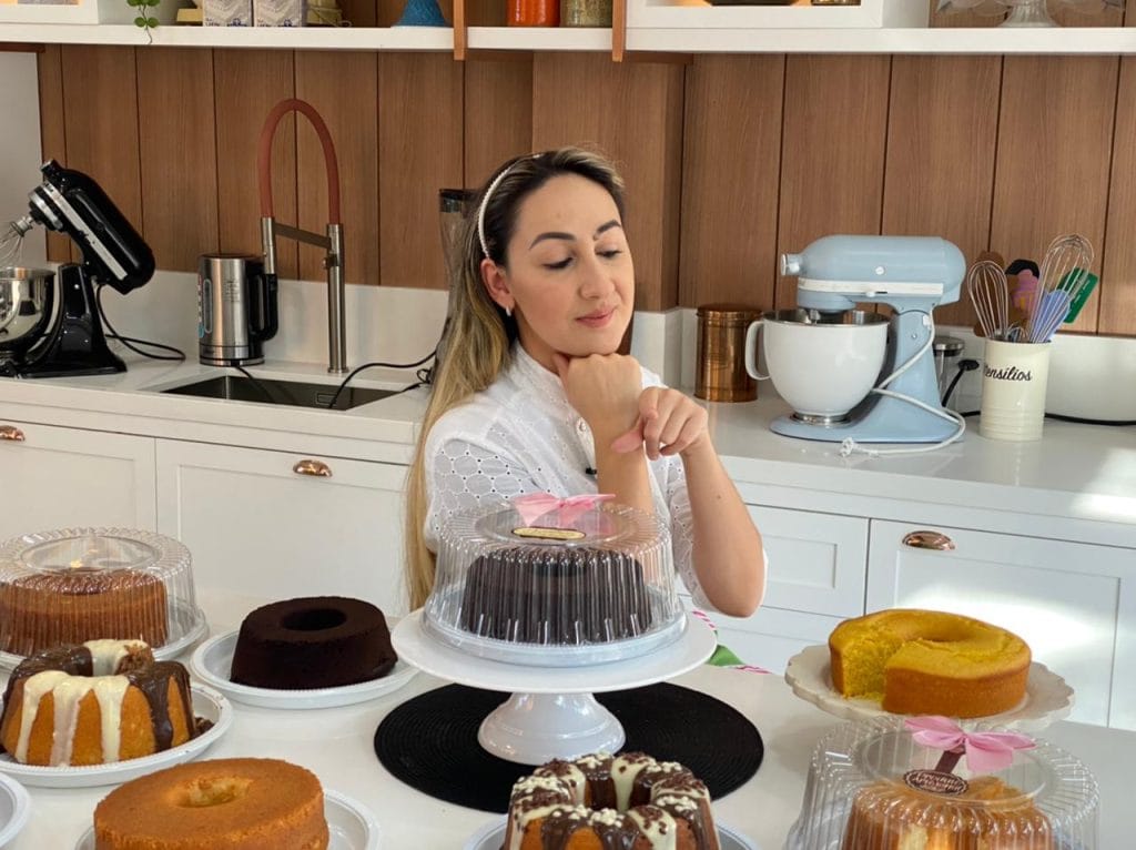Confeiteira especialista em cozinha moderna com batedeira, exibindo diversos bolos caseiros, incluindo bolo de chocolate e bolo de fubá, ensinados na apostila bolo caseiro da vovó