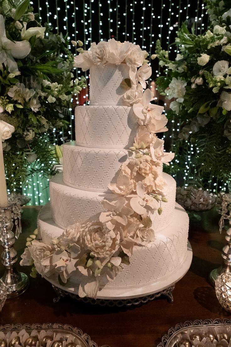 Bolo de casamento cake design branco com 4 andares, decoração luxuosa de flores de açúcar em cascata e acabamento em relevo, simbolizando a arte do designer de bolo