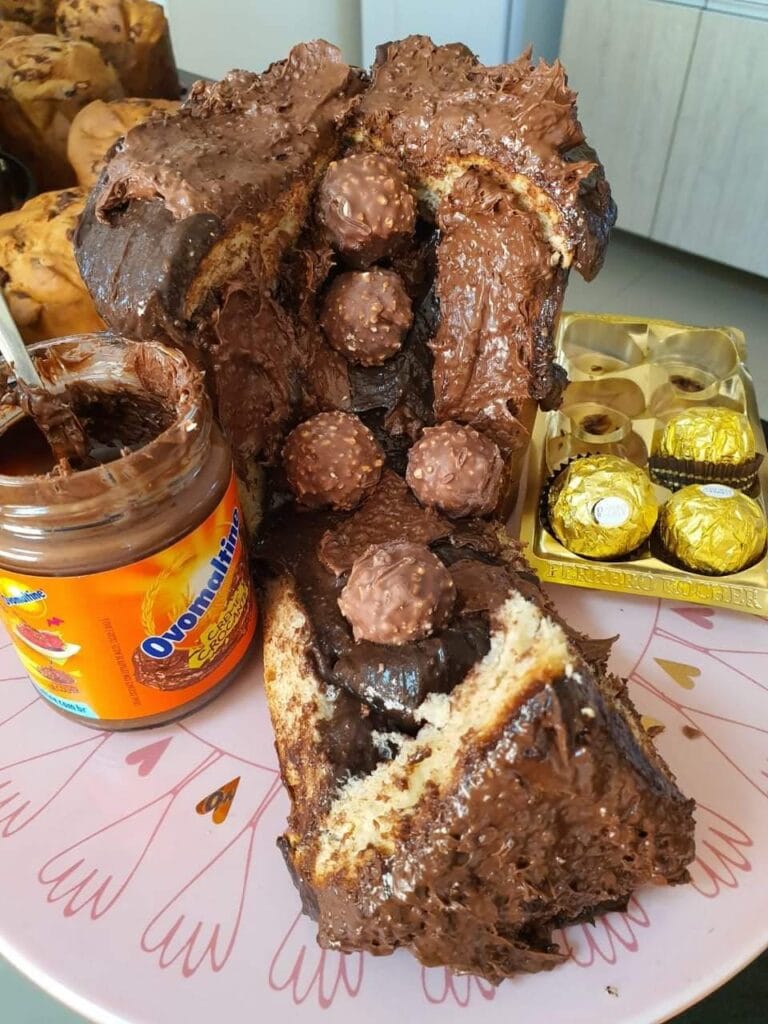 Chocotone recheado e cortado, mostrando o recheio de Ovomaltine escorrendo em abundância e decorado com bombons Ferrero Rocher. Este visual é essencial para campanhas de marketing de panetones gourmet.