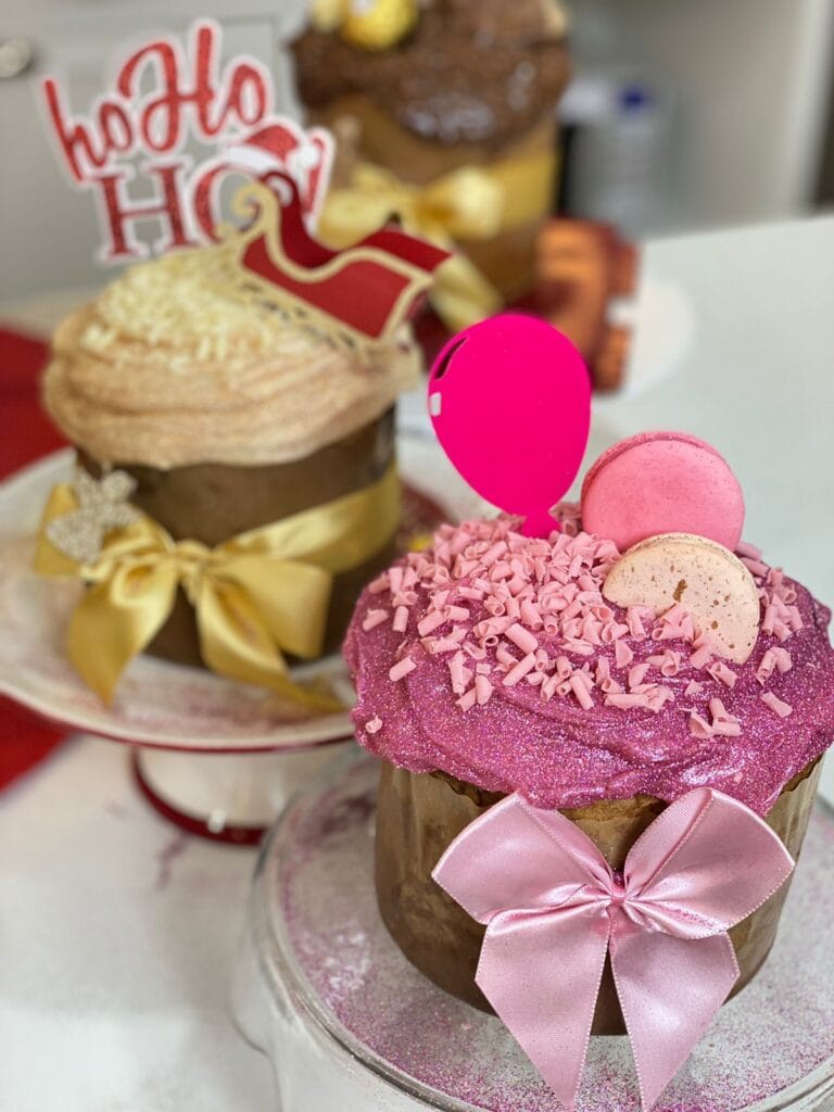Mini panetones trufados e decorados com temas de Natal, um com cobertura dourada e outro com brilho rosa e macarons. Ideal para kits presenteáveis e vendas de alto valor.