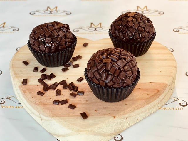 Três brigadeiros tradicionais cobertos com granulado de chocolate belga, prontos para vender.