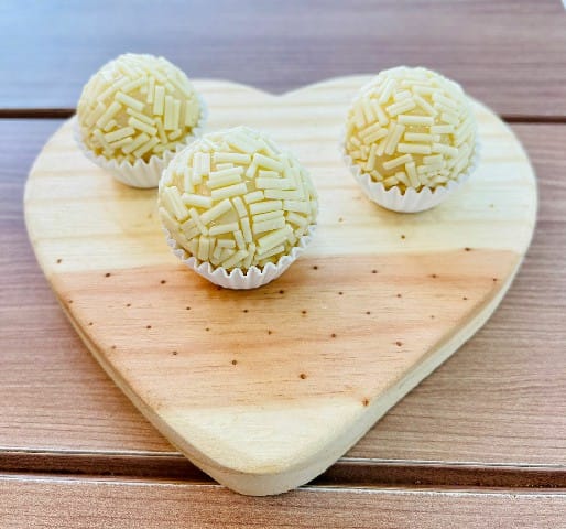 Três brigadeiros brancos cobertos com confeitos de chocolate branco. Exemplo de receita ensinada no curso de brigadeiros.