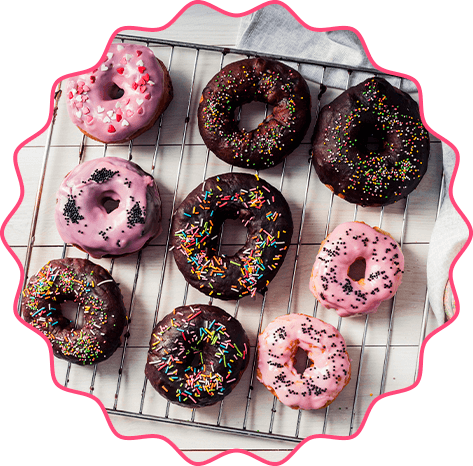 Nove donuts artesanais em uma grade, com coberturas de chocolate e glacê rosa e decoração de confetes e granulados, ensinados na apostila donuts gourmet