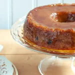 Pudim de pão cremoso e caramelizado, feito no liquidificador, desenformado em um prato de vidro com a calda de caramelo escorrendo. É uma receita de pudim de pão com leite condensado.