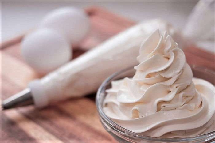 Tigela de Buttercream de Merengue Suíço de Limão liso e branco, com bico de confeitar e mangas de pasteleiro ao fundo. Ideal para cobertura para bolo de limão durinha.
