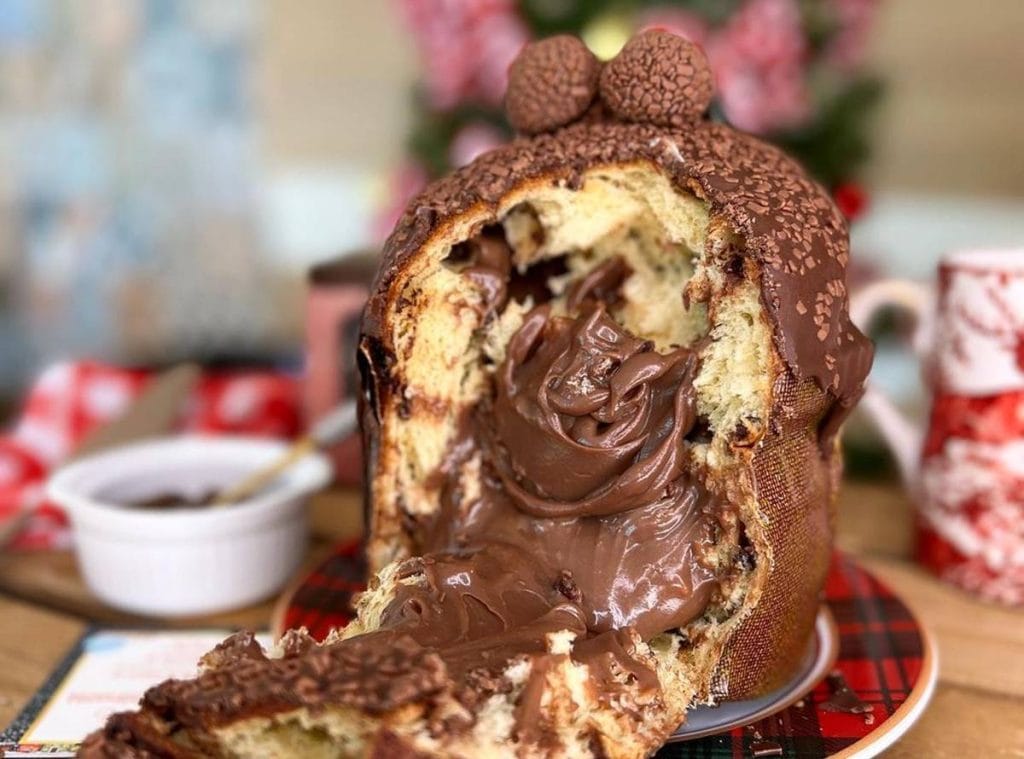Chocotone Vulcão cortado ao meio, com recheio cremoso de brigadeiro gourmet escorrendo e decoração com granulado e brigadeiros no topo. Ideal para vendas e fotos no Instagram.