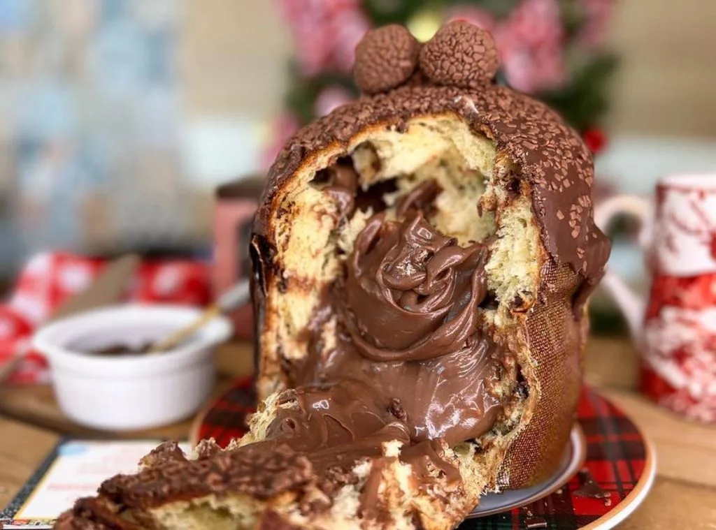 Chocotone Vulcão cortado ao meio, com recheio cremoso de brigadeiro gourmet escorrendo e decoração com granulado e brigadeiros no topo. Ideal para vendas e fotos no Instagram.
