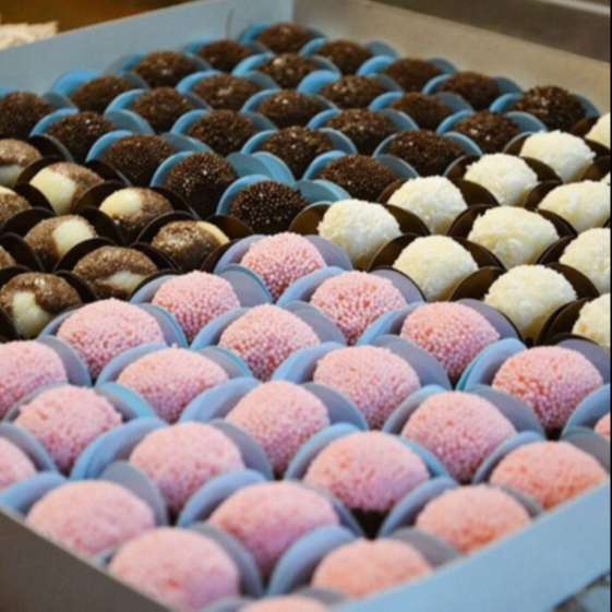 Caixa de doces finos com brigadeiros gourmet de chocolate, leite ninho e morango em forminhas azuis e rosas, conforme receitas da apostila brigadeiro gourmet